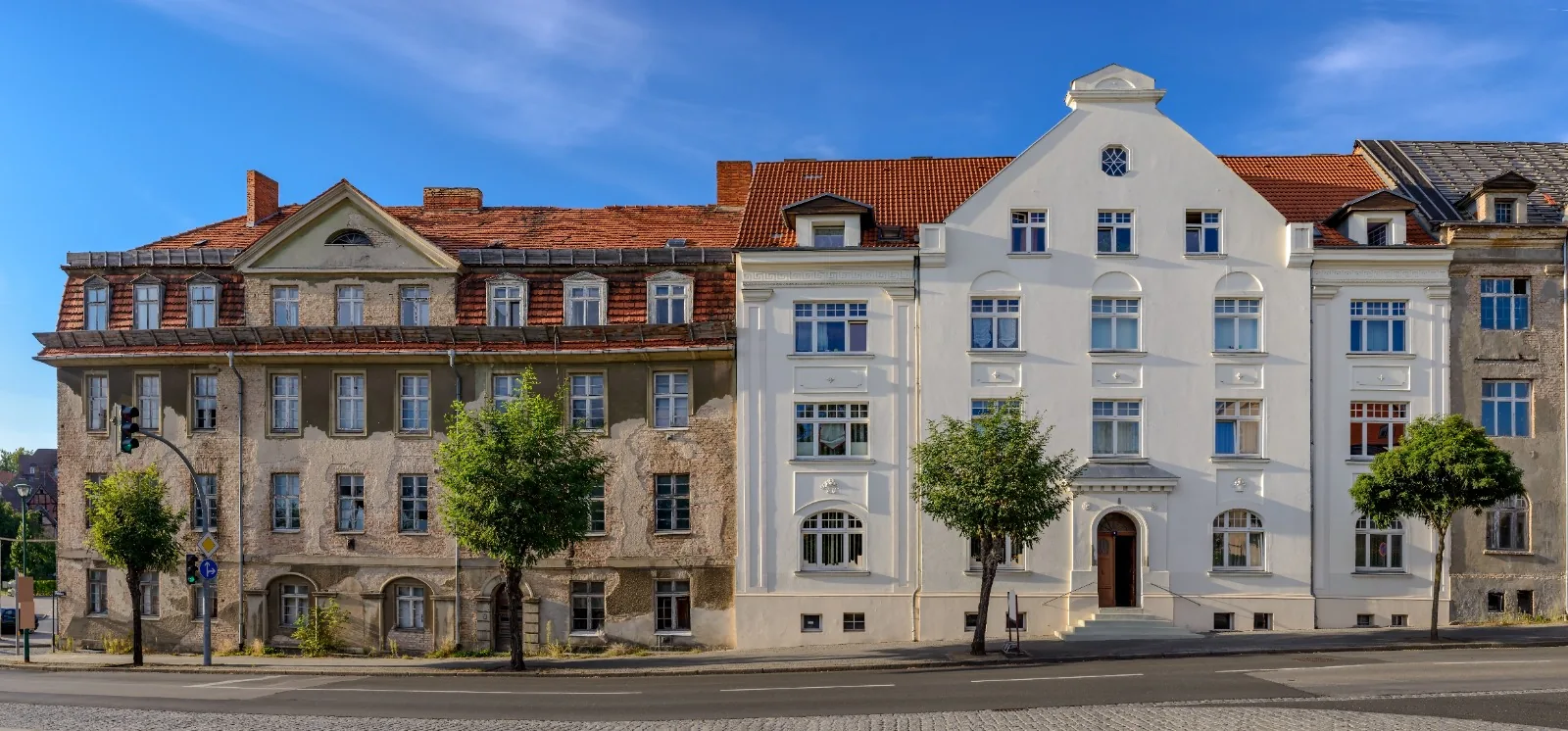 Zwei benachbarte Altbaufassaden: links eine unsanierte Fassade mit abblätterndem Putz, rechts eine frisch sanierte helle Fassade.
