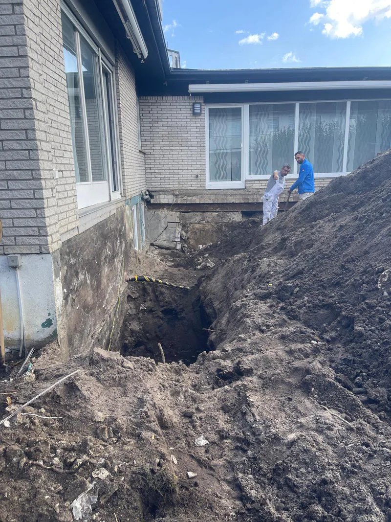 Offene Baugrube neben einem Wohnhaus mit einem großen Erdaushub, im Hintergrund die freigelegte Kellerwand.