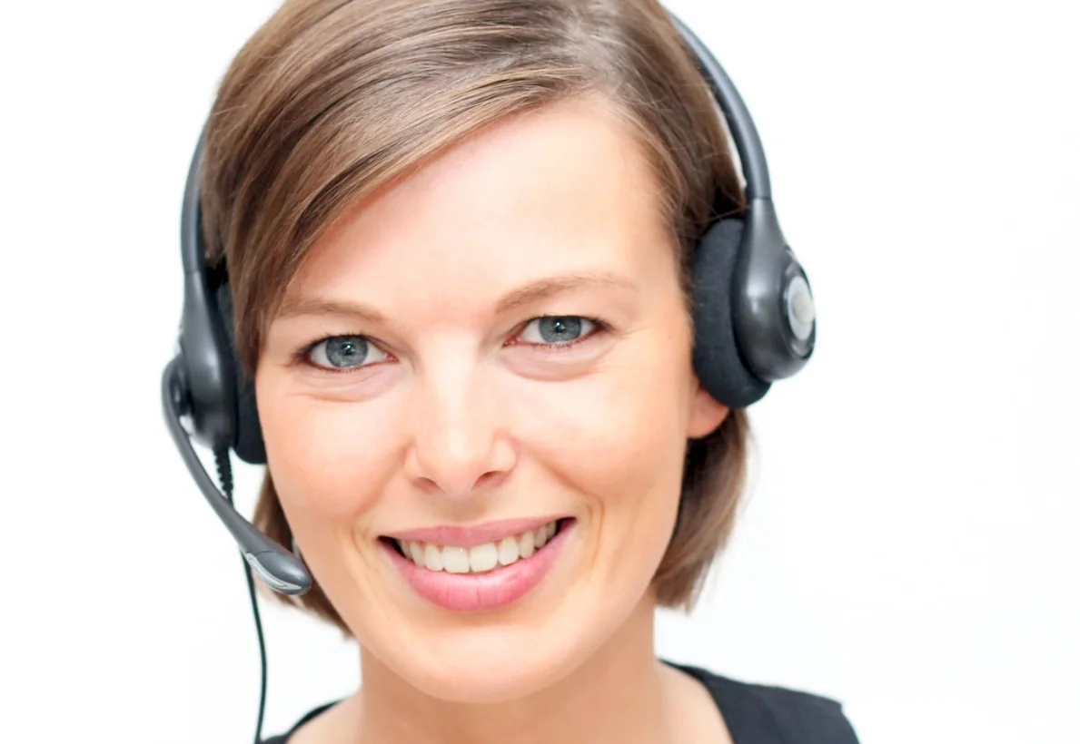 Lächelnde Frau mit Headset vor weißem Hintergrund.