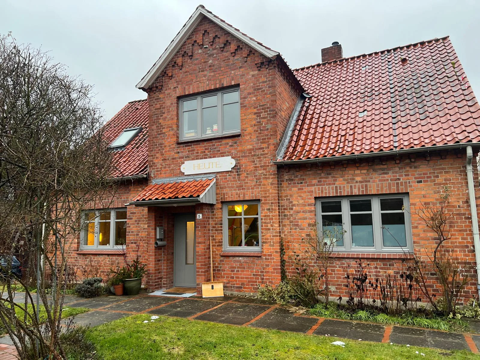 Freistehendes Wohnhaus mit roter Backsteinfassade, grauen Fenstern und rotem Ziegeldach.