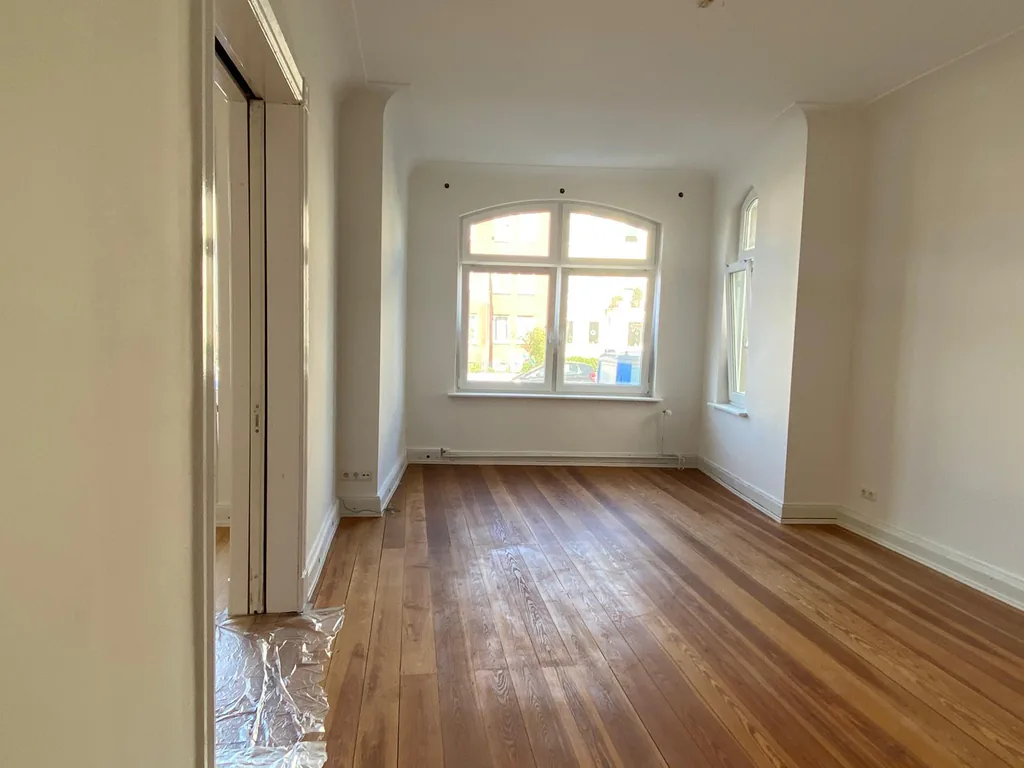 Fertig sanierter Wohnraum mit Dielenboden, hellen Wänden und einem Rundbogenfenster.