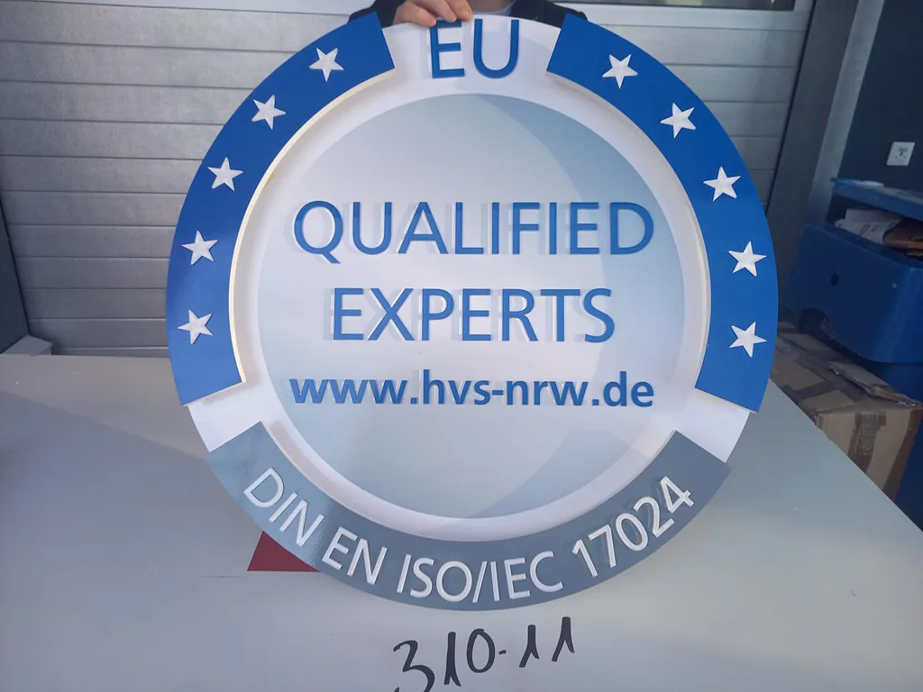 Rundes Schild mit blauem Sternenkranz und der Aufschrift „EU Qualified Experts, www.hvs-nrw.de“ sowie „DIN EN ISO/IEC 17024“ am unteren Rand.